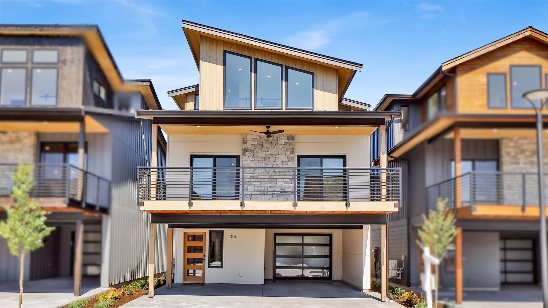 Modern two-story house with angled rooflines, stone accents, large balcony, and glass garage door